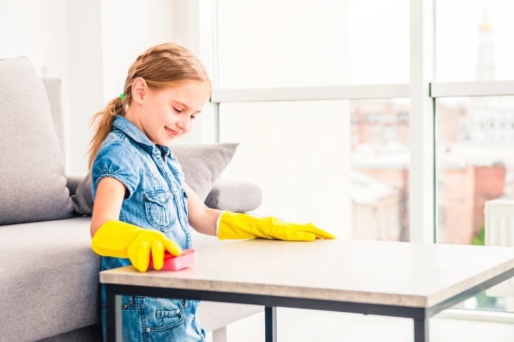 little girl wiping a table while wearing yellow rubber gloves