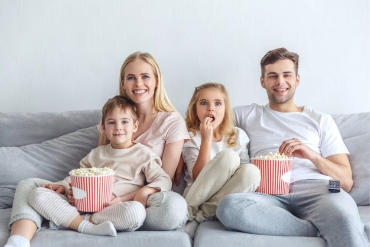 family watching a movie together on the couch while eating popcorn