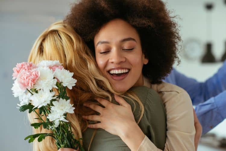 woman hugging another woman while holding a bouquet of flowers