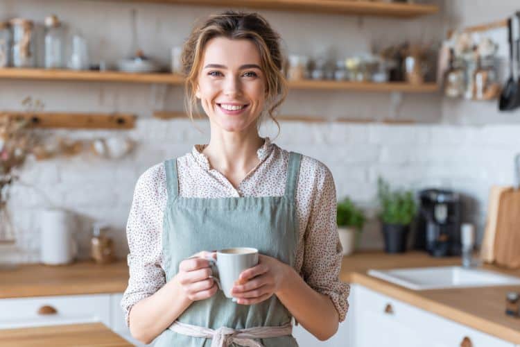 smiling woman standing a kitchen drinking coffee